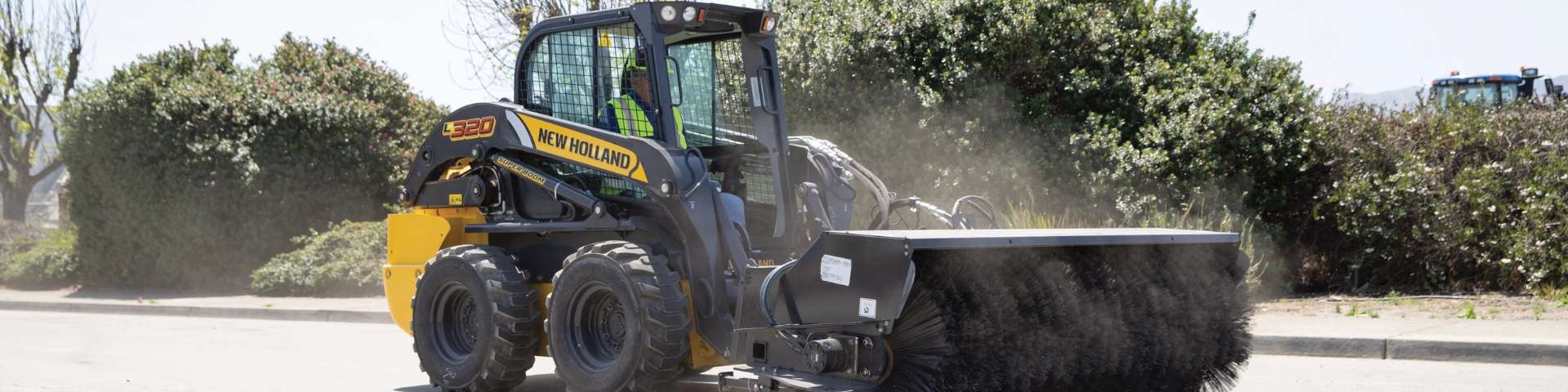 Skid steer loader sweeping street with broom attachment.