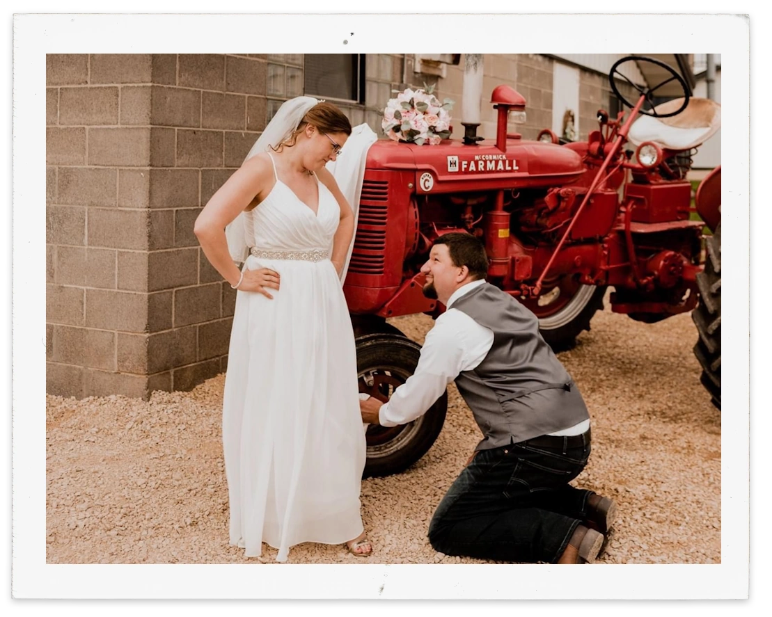 Cody K untangling his bride's dress from the tire of vintage Farmall farm equipment.