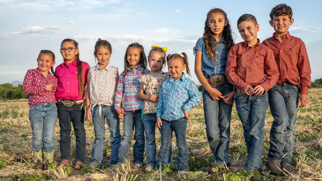 9 smiling children standing in a field.
