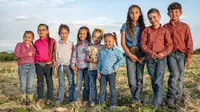 9 smiling children standing in a field.