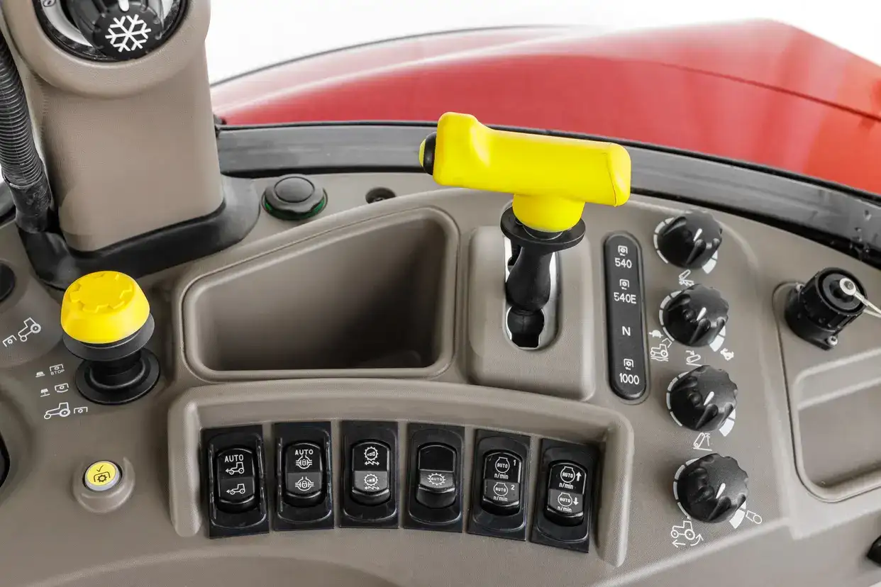 Close-up of a Case IH Farmall Utility tractor control panel featuring various buttons, knobs, and a yellow joystick for operation.