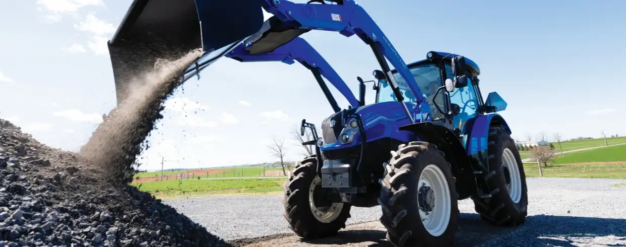 WORKMASTER PLUS tractor with a bucket dumps rocks into a pile.