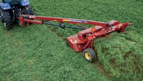 Red disc mower-conditioner mowing grass.