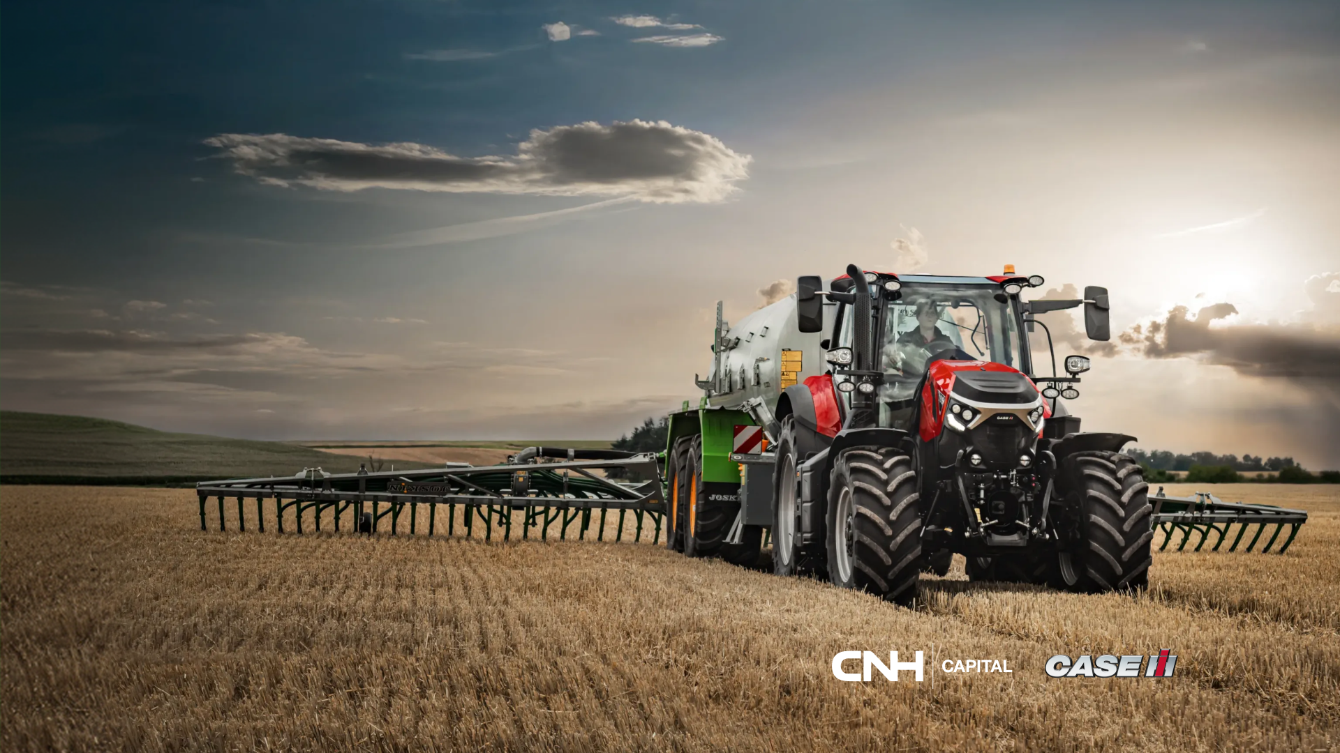 Trattore Case IH rosso al lavoro in un campo di stoppie al tramonto sotto un cielo nuvoloso