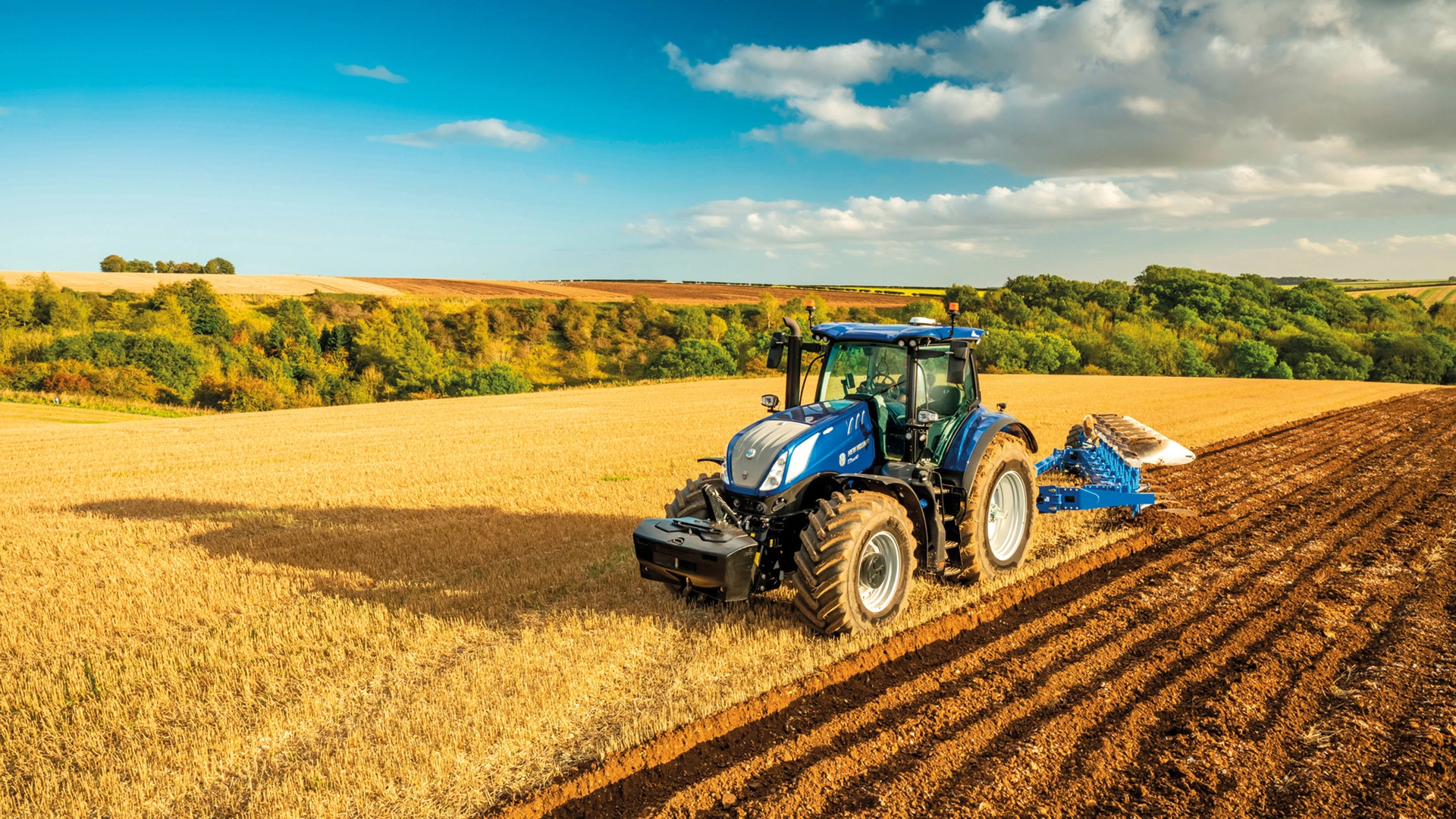 New Holland tractor with a reversible plough tilling golden farmland