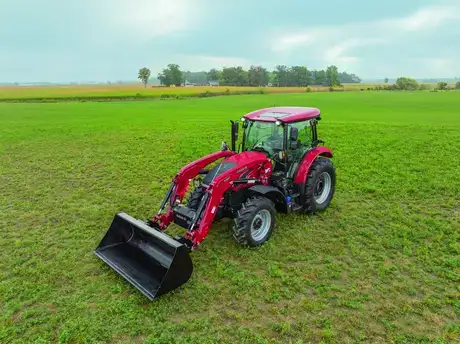 A Case IH Farmall tractor with a front loader stands on a vast green field under a cloudy sky, conveying rural tranquility and agricultural productivity.