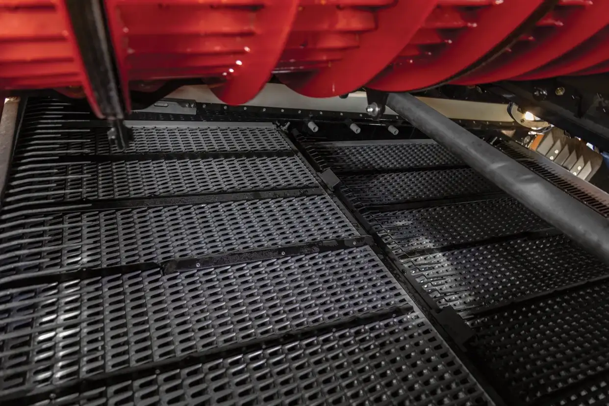 Interior view of a combine cleaning system showing perforated cleaning sieves beneath the rotor for grain separation.