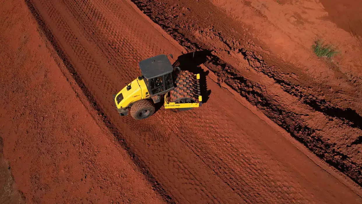 outdoor photo of the New Holland Construction road roller in operation, viewed from above, on red earth.