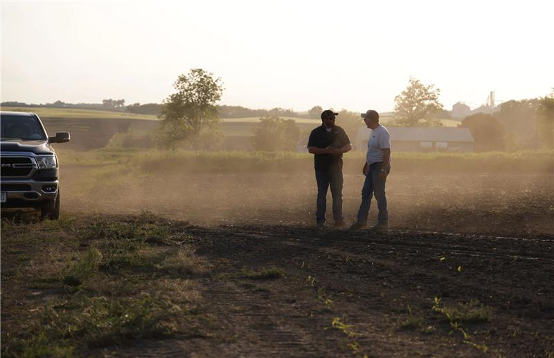 Two farmers talking in a dusty field near a truck.