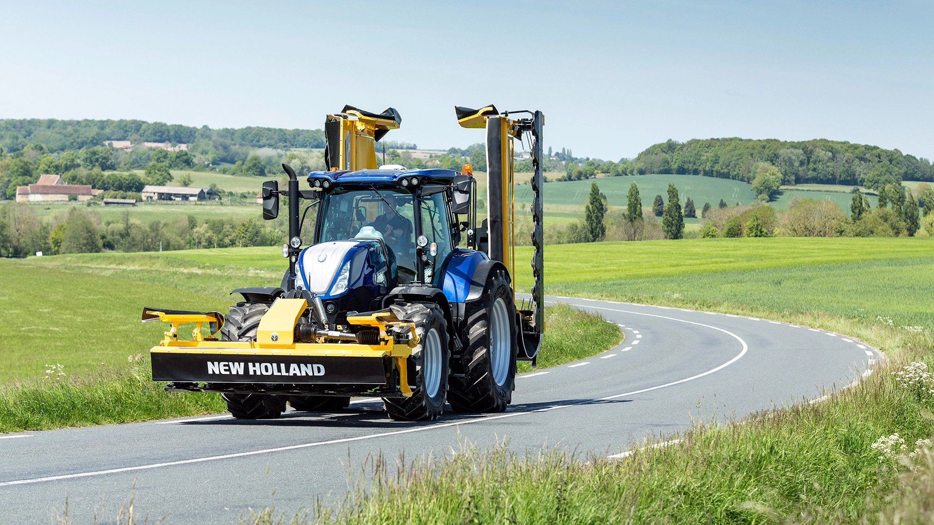 T7 SWB Tractor transporting mounted mowers on the road