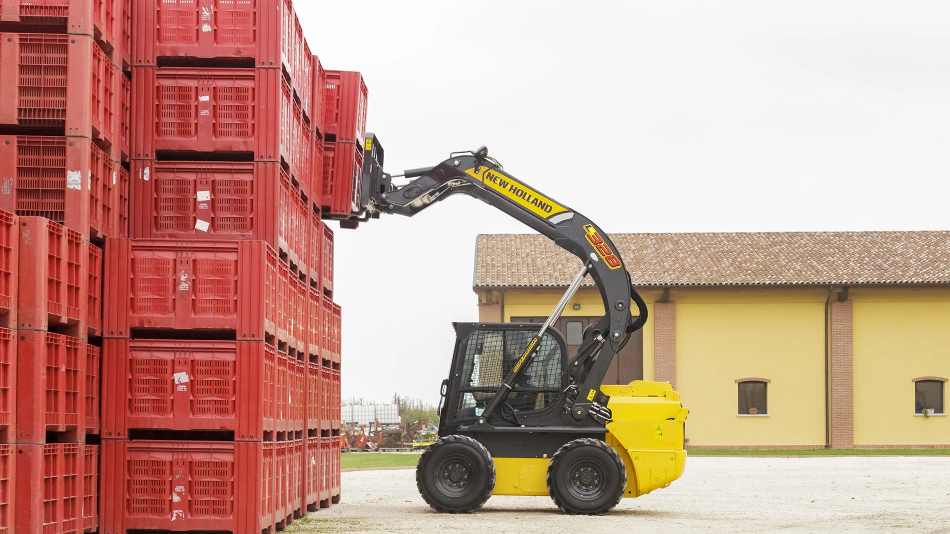New Holland Skid Steer Loader stacking red crates outside a warehouse with clay-tiled roof.