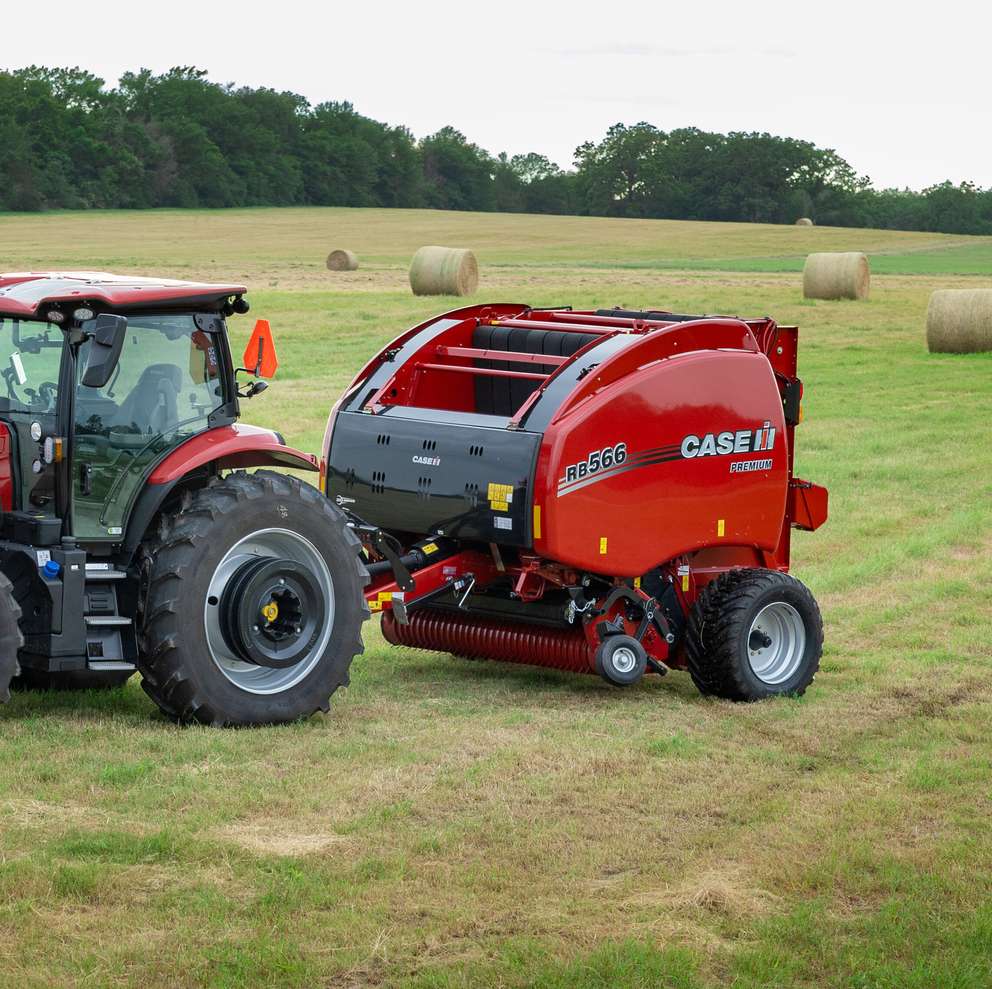 Case IH Maxxum 150 tractor towing a red RB566 round baler in a hay field with rolled bales scattered across the background.