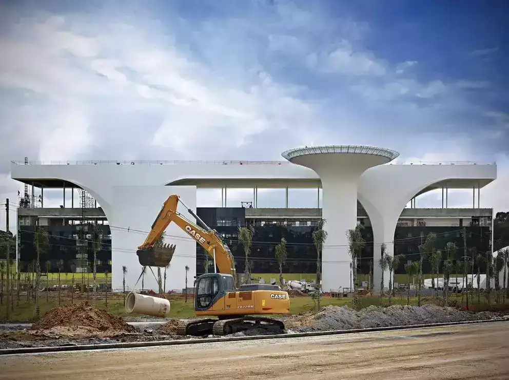 foto ao ar livre da escavadeira hidráulica da Case Construction posicionando um tubo de drenagem na trincheira de uma grande construção elaborada por Oscar Niemeyer.