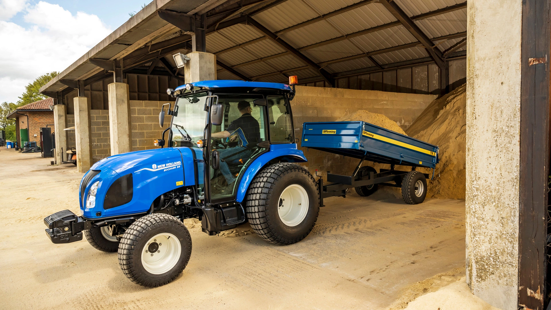 New Holland Boomer tractor with trailer moving sand across the farm