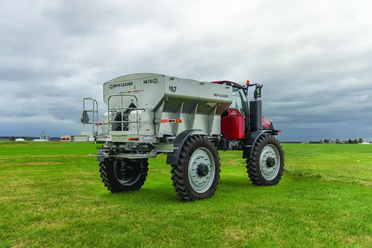 A red and silver Case IH agricultural spreader vehicle stands on a vast green field under a cloudy sky, conveying a sense of modern farming and open space.