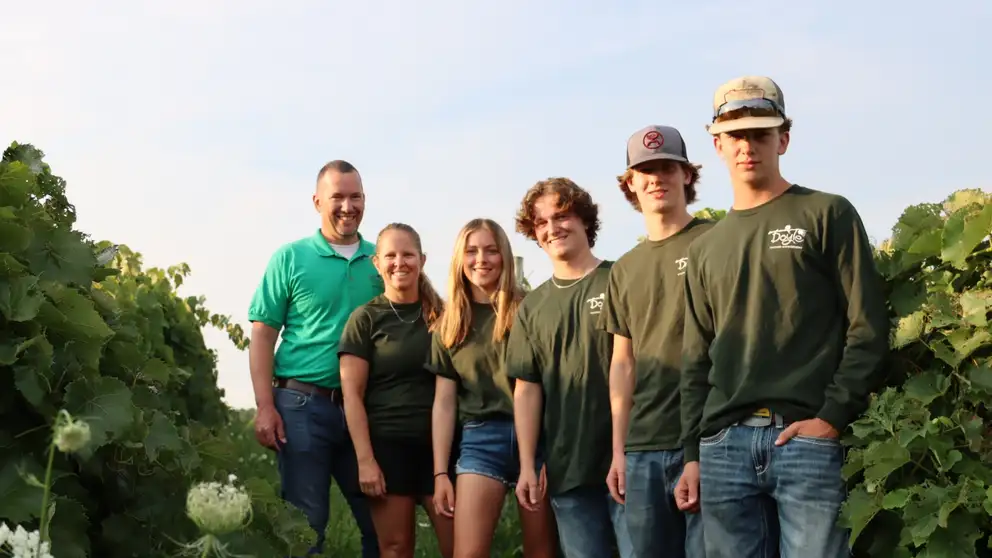 Family of 6 standing next to flowers and leaves.