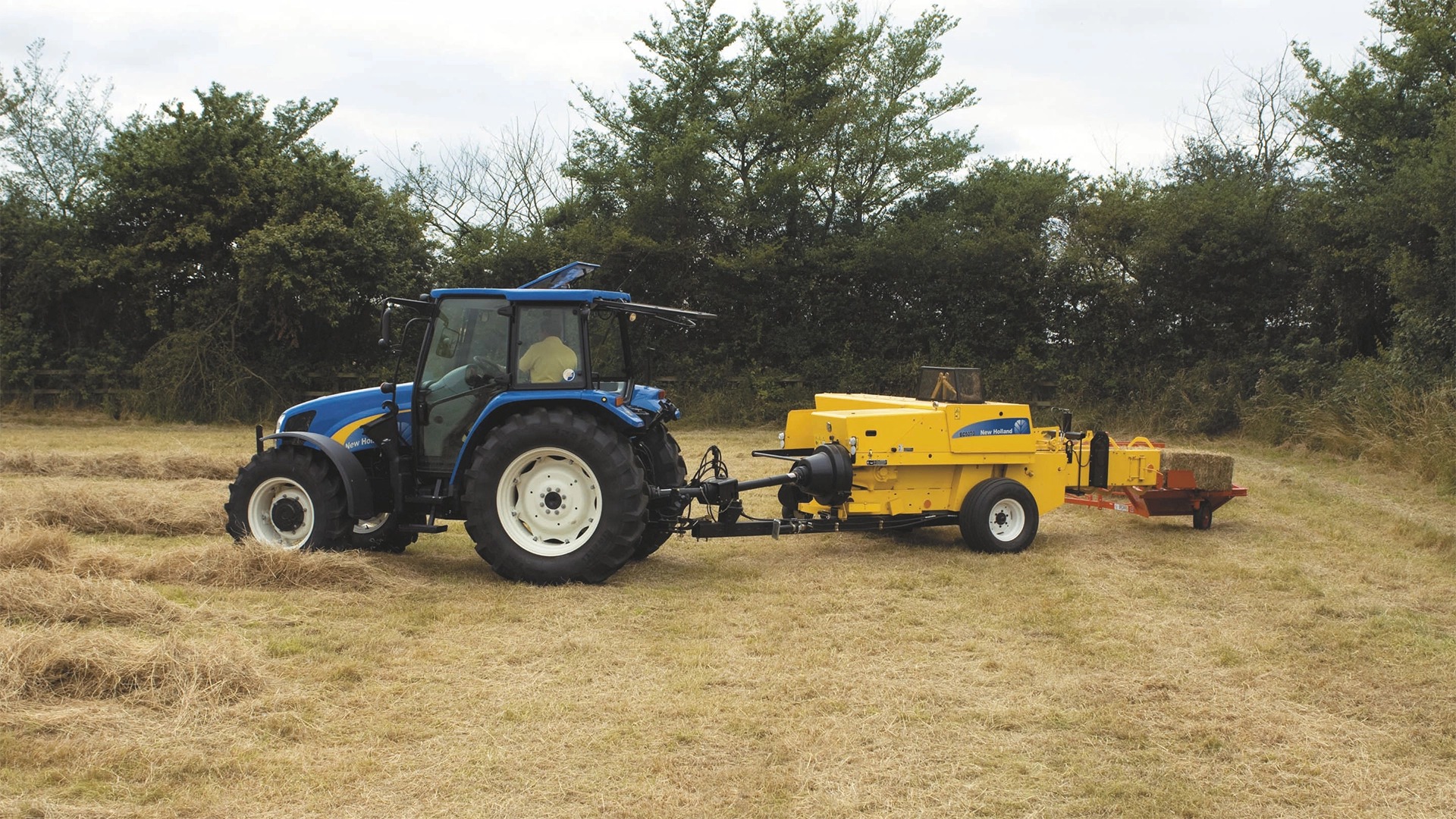 New Holland tractor towing a BC5000 baler through a hay field.