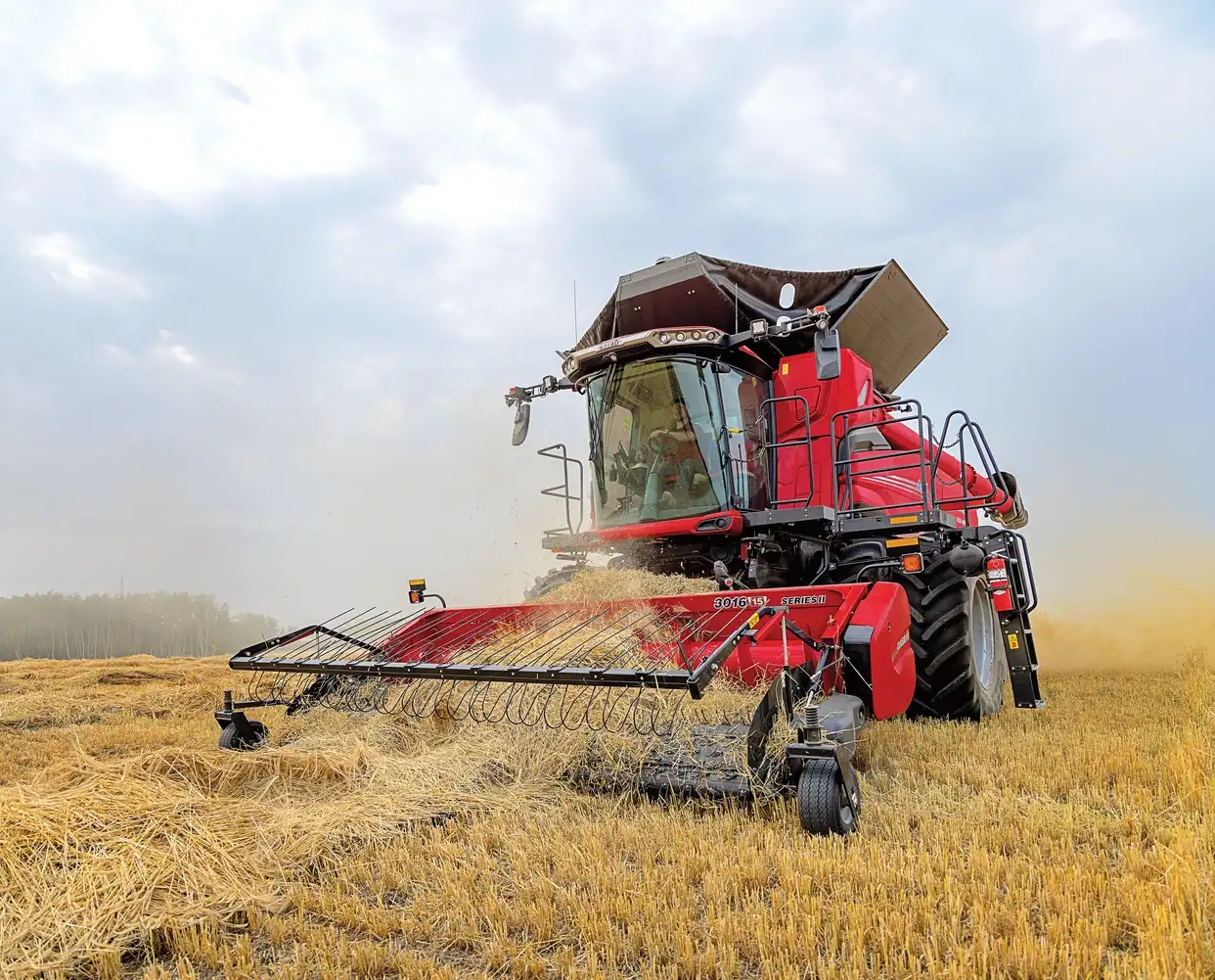 A red Case IH combine harvester cutting through a wheat field, with dust and chaff being kicked up around it as it works.