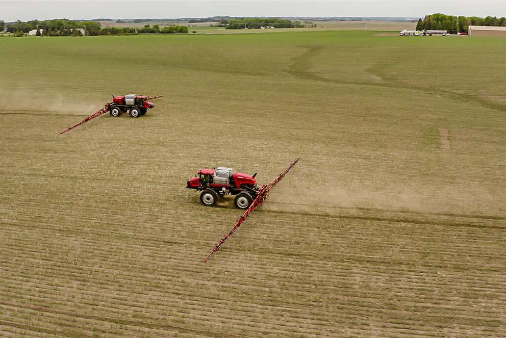 Two red Case IH sprayers working in a large farm field.