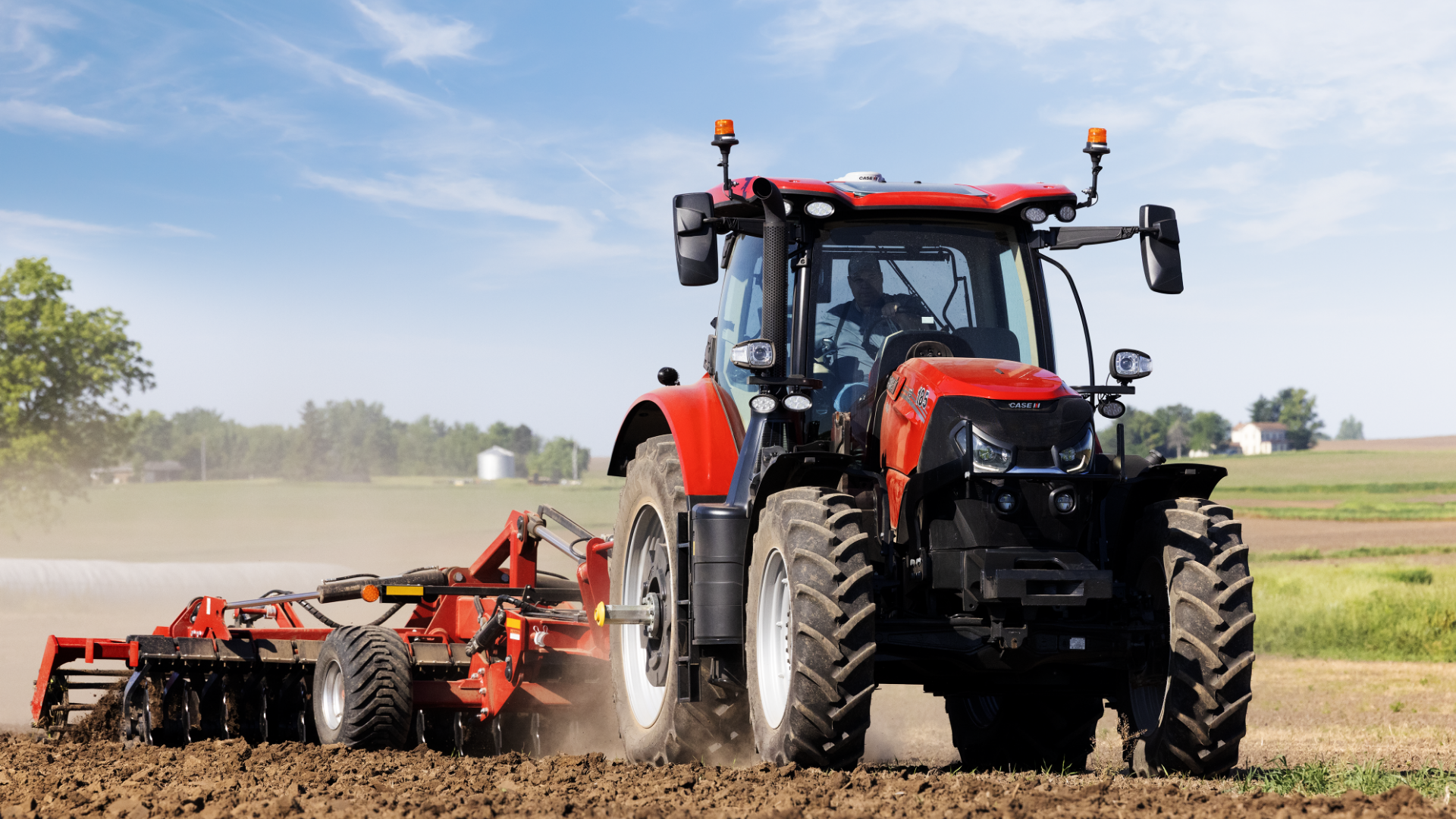 A Case IH tractor plows a vast, earthy field under a clear blue sky, evoking a sense of rural productivity and calm. 