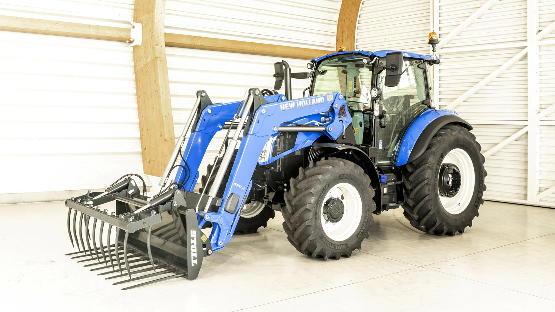 Blue New Holland tractor equipped with a loader grapple bucket, displayed indoors.