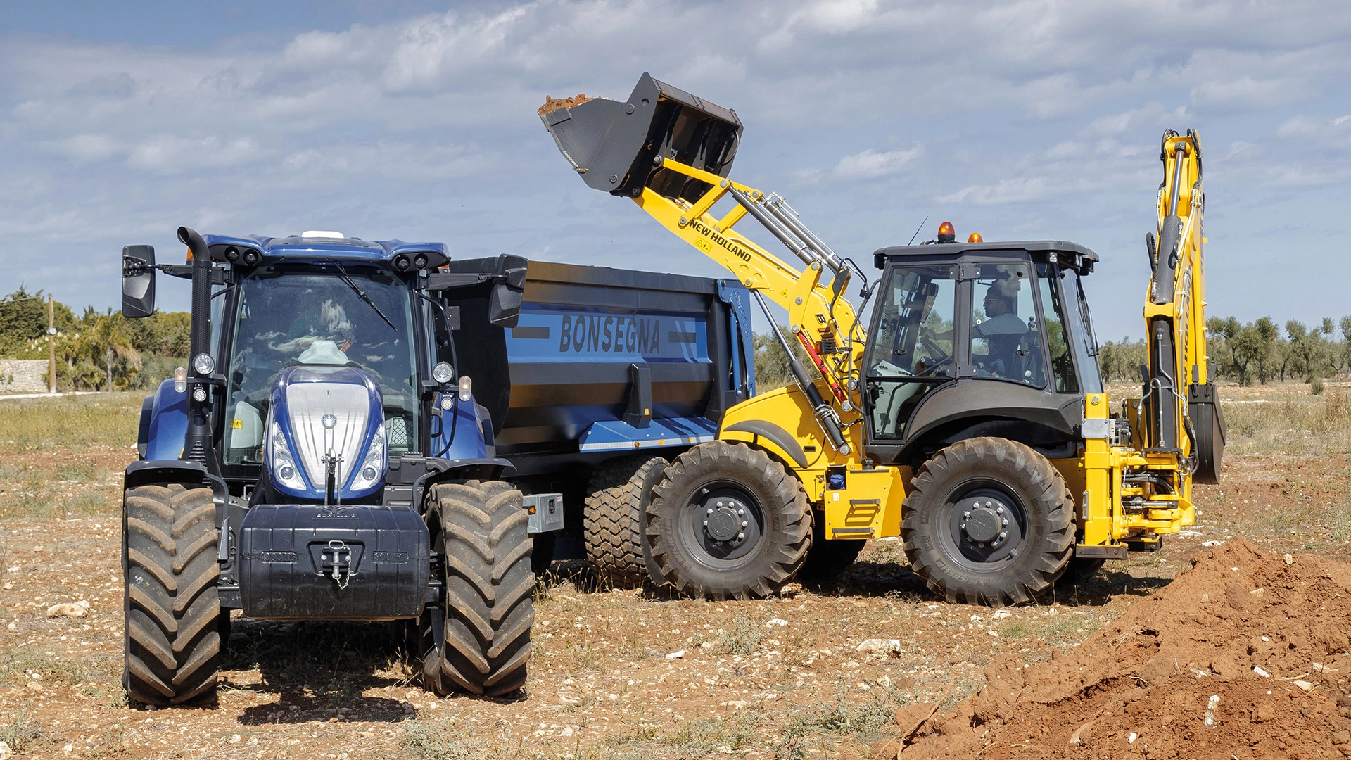 New Holland tractor & backhoe at work, loading soil into a trailer on a clear field day.