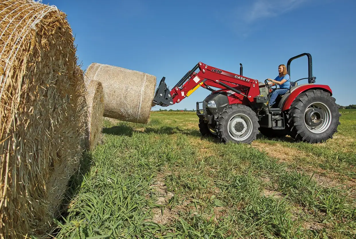 Woman driving a Farmall Utility 75A tractor with L610 Loader with wrapped hay.