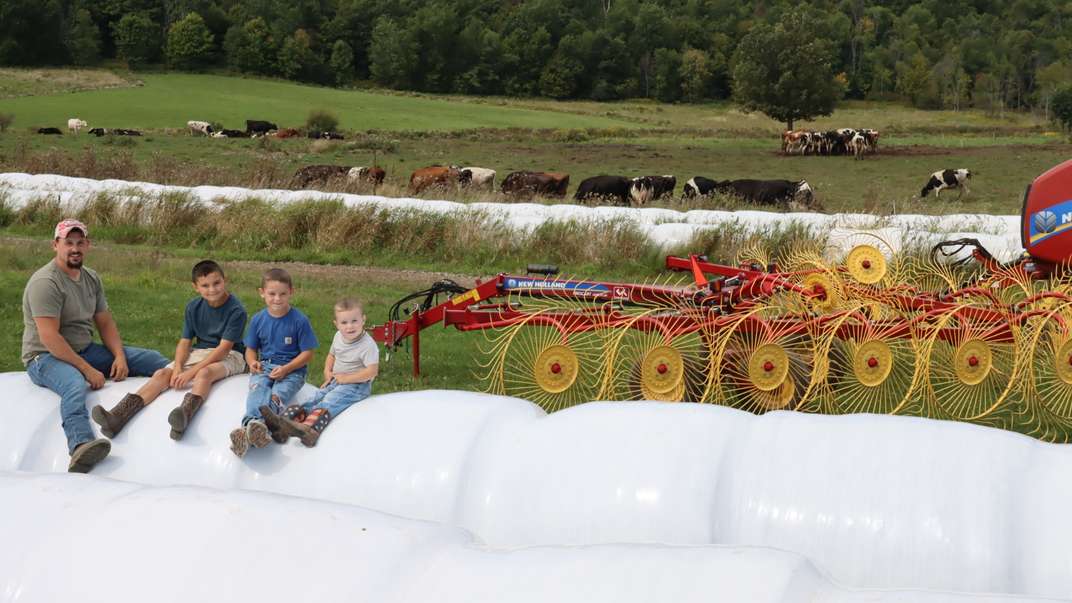 Family of 4 sit in front of New Holland Hay Rakes and cows.