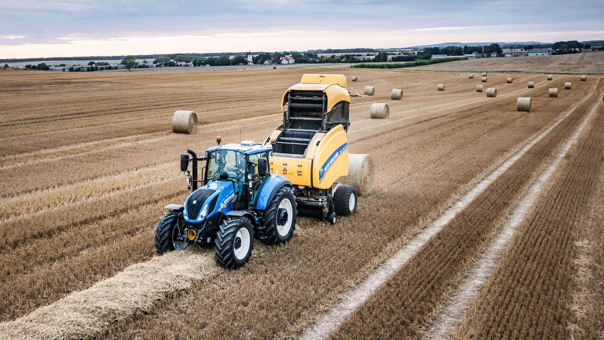 Tractor in action, operating a Roll-Belt round baler on an expansive agricultural field