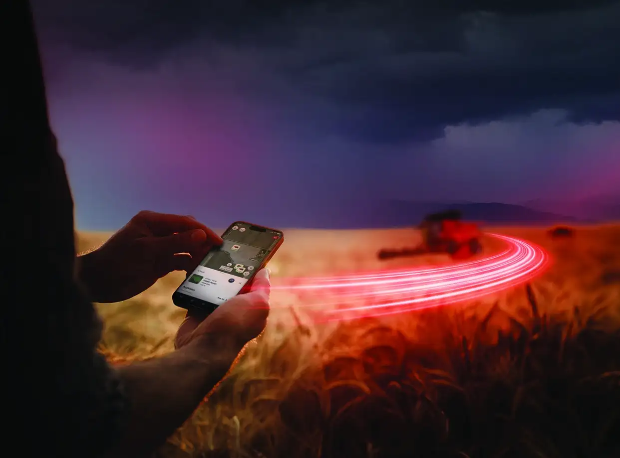 A person uses a smartphone with FieldOps in a wheat field at dusk. A tractor emits glowing red tracks, creating a futuristic atmosphere.