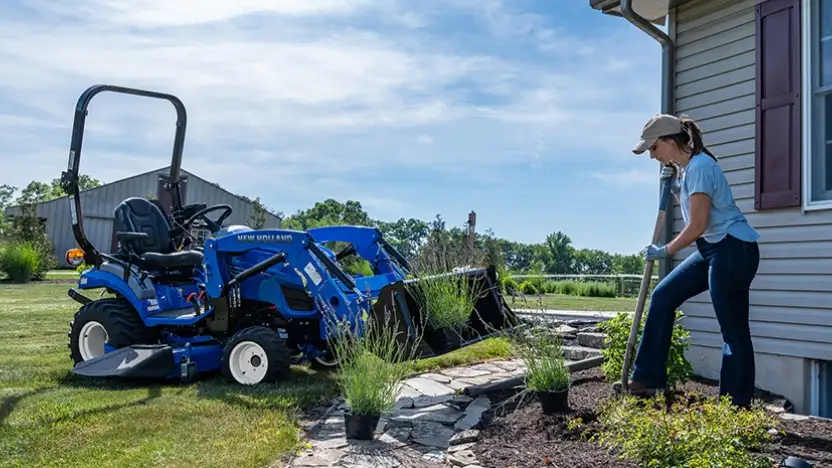 Woman with a shovel next to a blue tractor.
