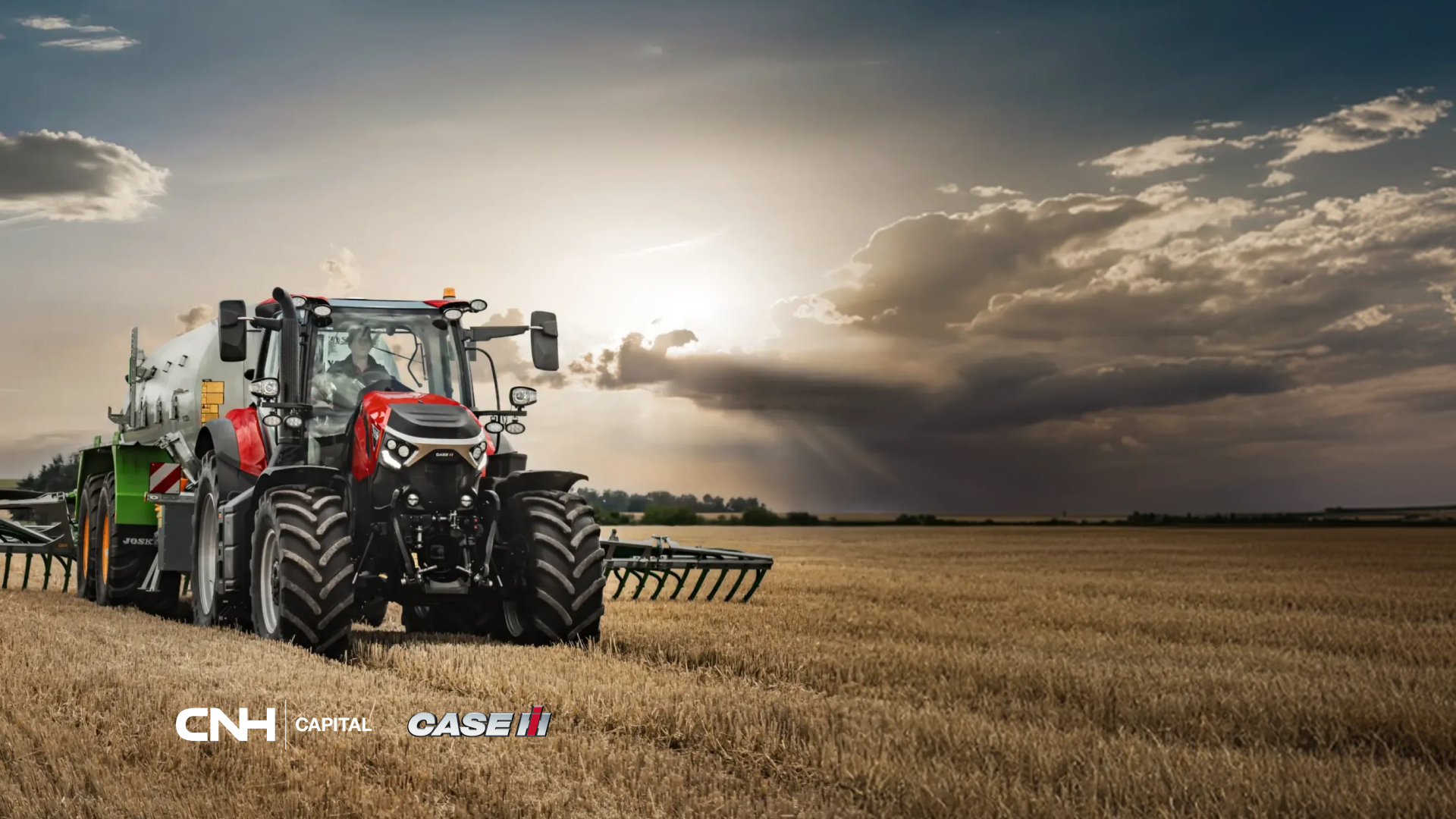 Trattore Case IH rosso al lavoro in un campo di stoppie al tramonto sotto un cielo nuvoloso