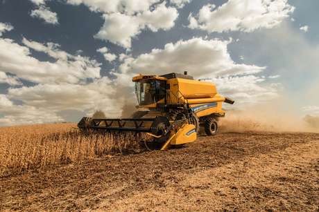 foto ao ar livre, com destaque para a lateral da colheitadeira da New Holland trabalhando em um vasto campo.