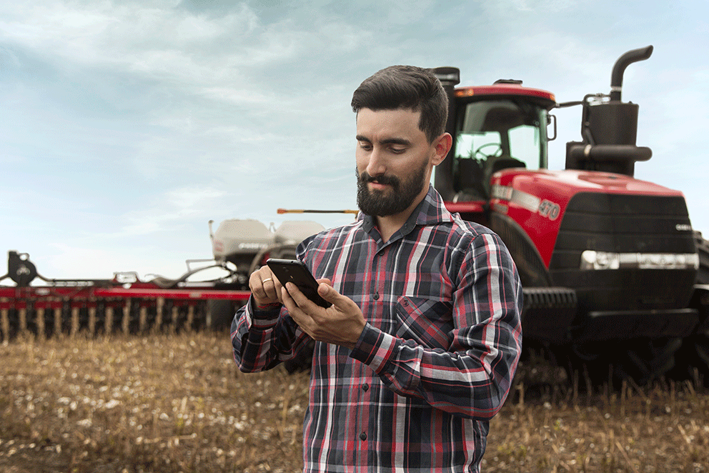 Homem-mexendo-em-tablet-no-campo-com-máquina-ao-fundo.png