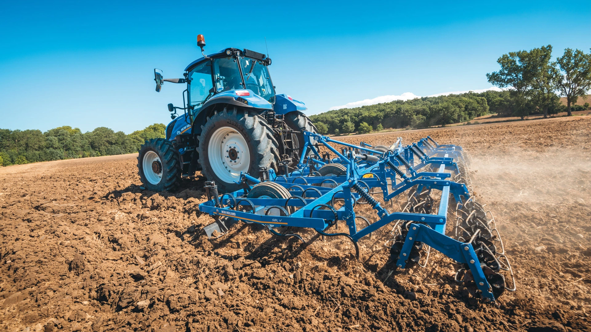 Active New Holland tractor with spring tine cultivators tilling the soil