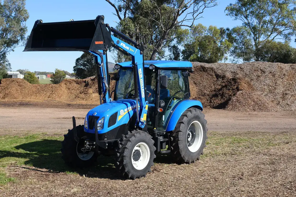 Blue New Holland TT4 Tier 3 tractor in field with loader and 4 in 1 bucket attached