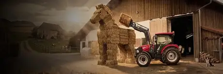 Case IH Traktor mit Frontlader baut eine Pferdeskulptur aus Strohballen vor einer Scheune