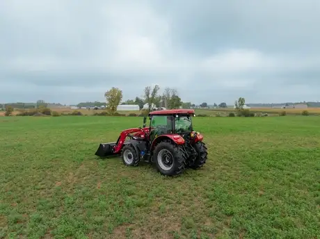 A Case IH Farmall tractor sits in the middle of a lush green field under a cloudy sky, conveying a sense of calm and readiness for agricultural work.