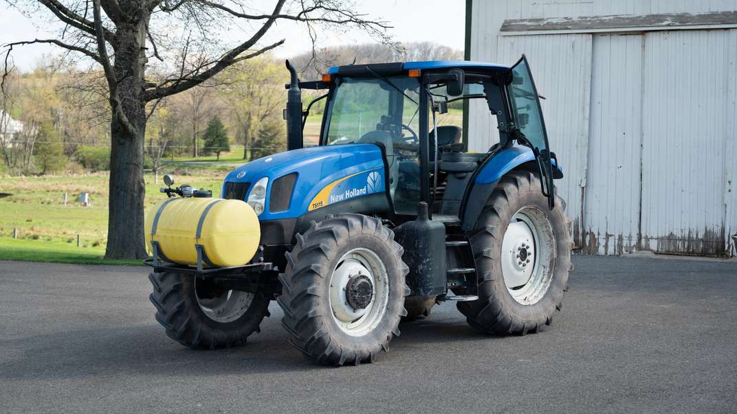 Diagonal profile of New Holland TS115A Tractor in front of a shed.