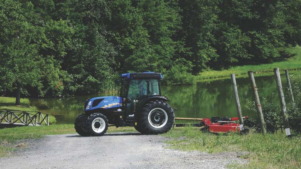 A New Holland tractor pulls an implement in an orchard