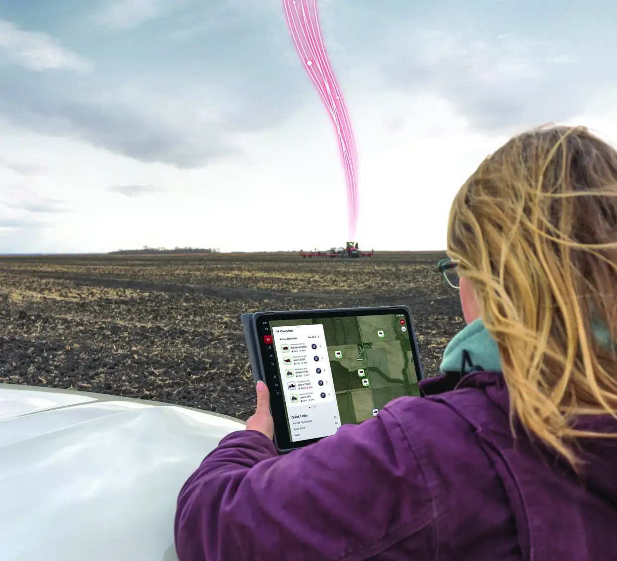 Woman looking at real time fleet GPS data on tablet with farm equipment in the distance.