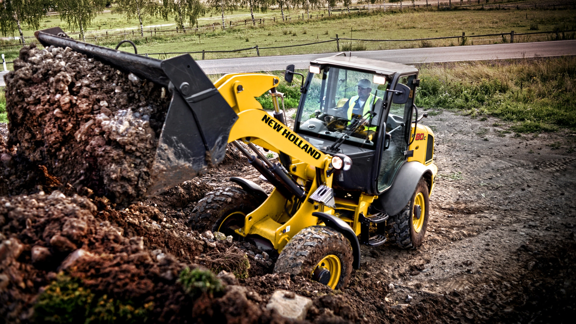 New Holland compact wheel loader in action, scooping up mixed soil on a construction site.