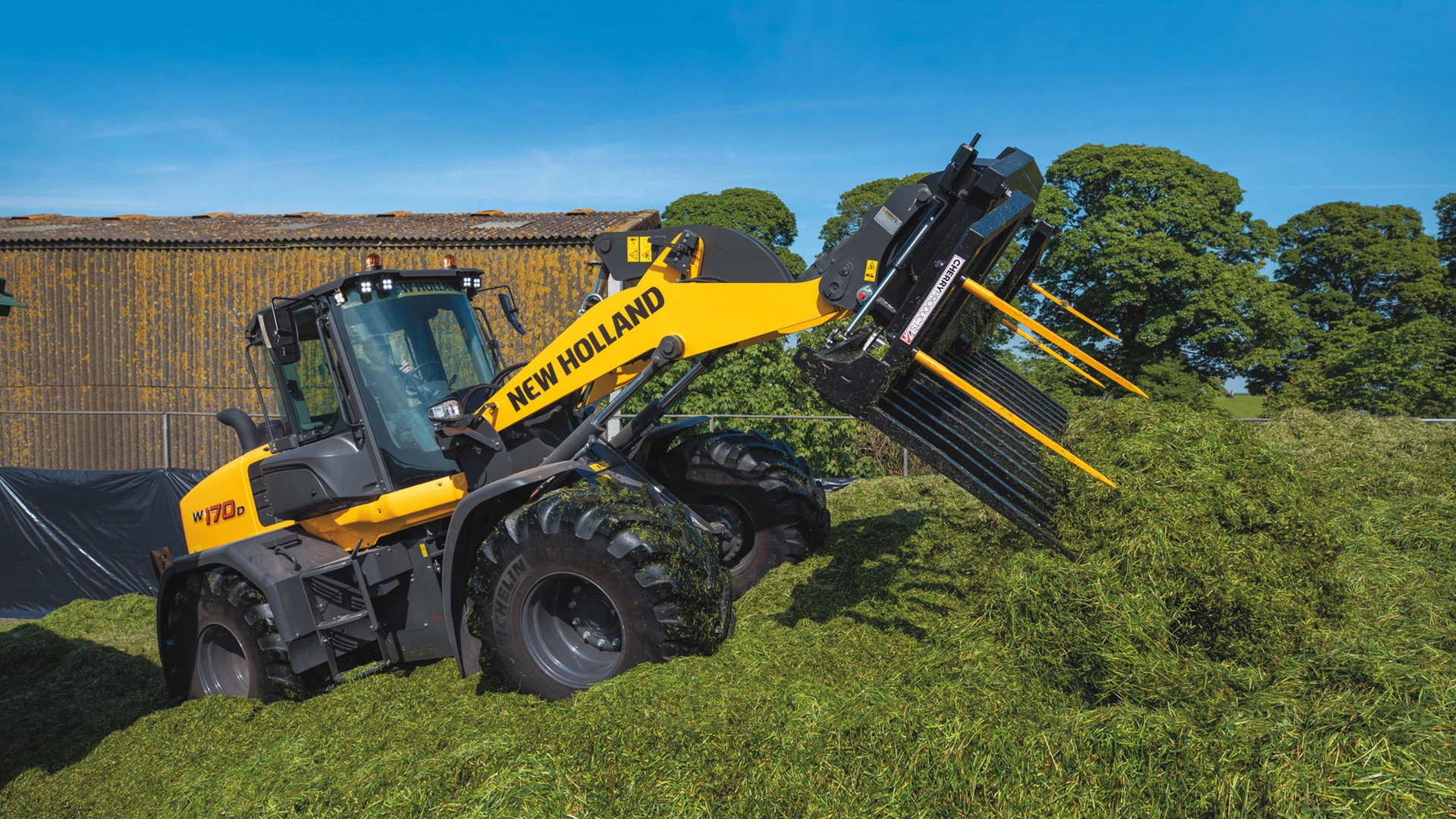 New Holland W170D wheel loader in action, lifting fresh green silage against a clear blue sky, showcasing advanced farming machinery and agricultural efficiency.