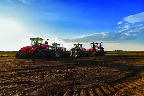 Four red Case IH tractors line up across a freshly plowed field beneath a vast blue sky.