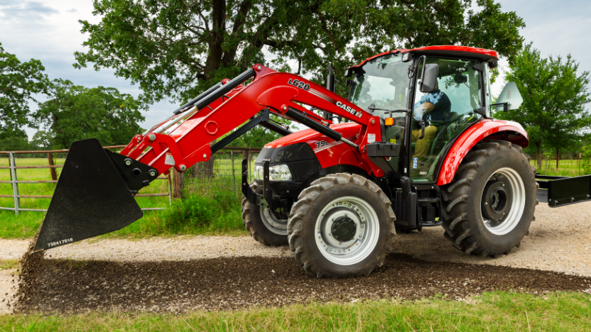 A Case IH tractor with a front loader scatters gravel on a dirt path in a green field.
