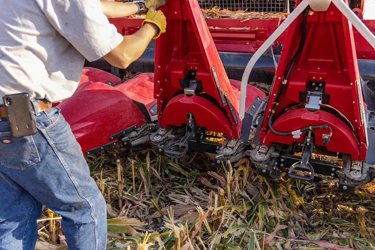 A person in jeans and gloves adjusts the Case IH C500 series on a field strewn with corn stalks, highlighting farm equipment in use.